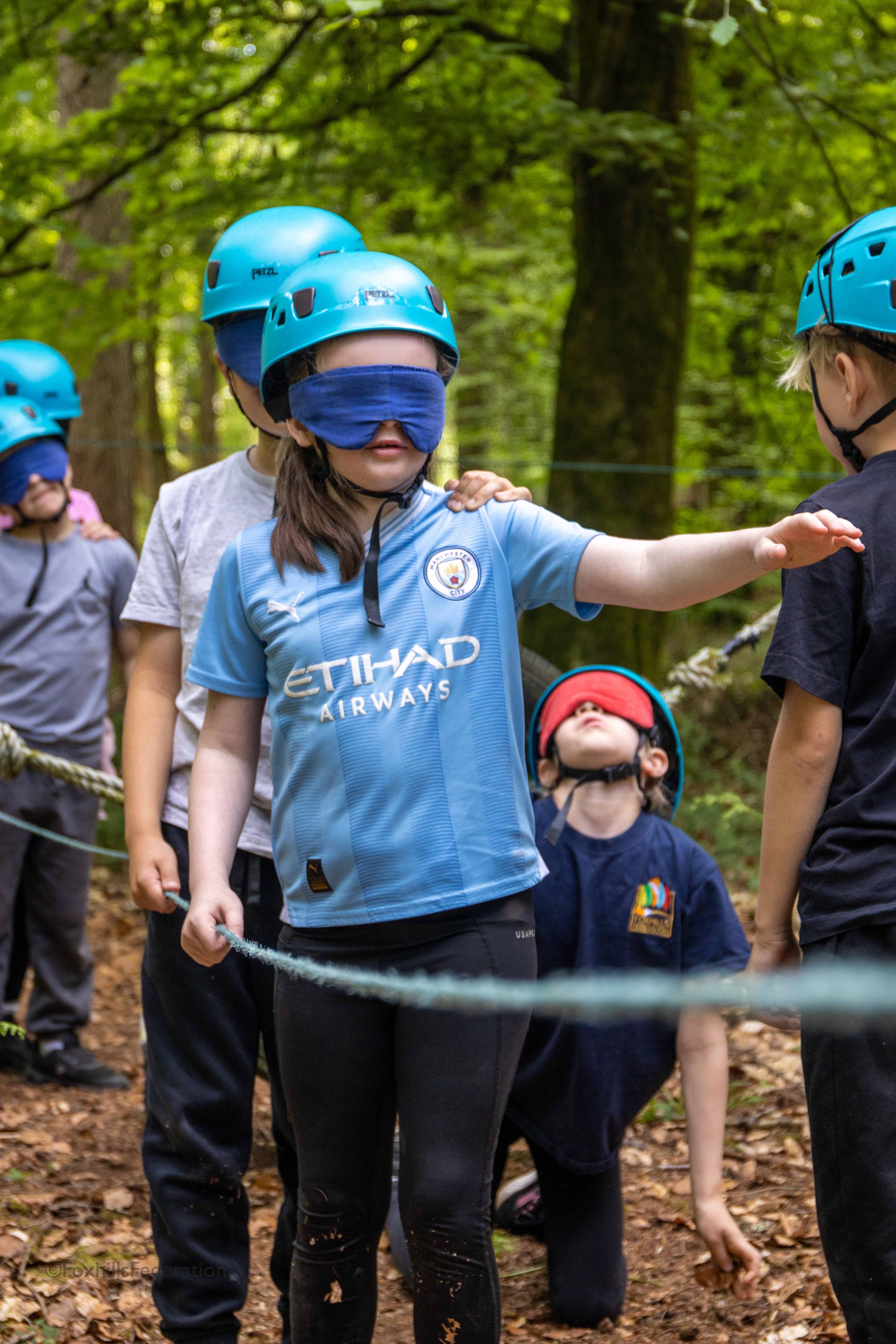 A blindfolded girl leads a group of children through a trail